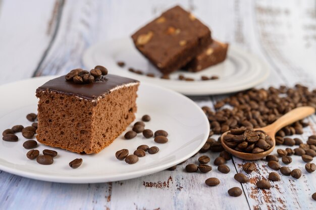 Bolo de chocolate em um prato branco e grãos de café em uma colher de pau em uma mesa de madeira.