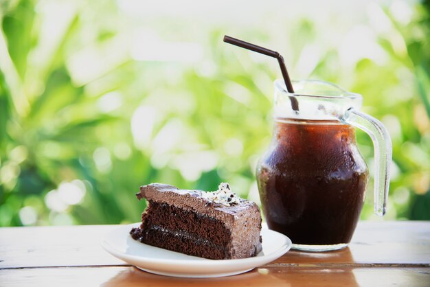 Bolo de chocolate na mesa com café gelado sobre jardim verde - relaxar com bebidas e padaria no conceito de natureza