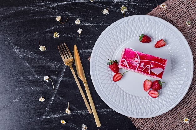 Bolo de frutas com morangos em um prato branco com talheres de ouro.