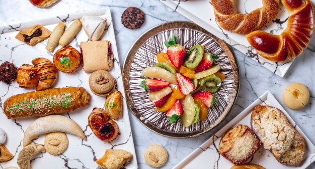 Bolo de frutas vista superior com creme de baunilha chocolate kiwi abacaxi morango laranja e bolos em cima da mesa