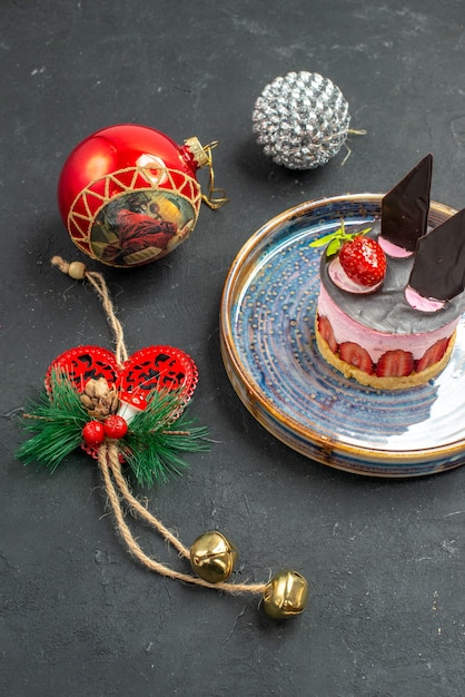 Bolo de queijo delicioso com morango e chocolate em prato oval de árvore de natal - brinquedos de árvore de natal em fundo escuro isolado - vista frontal