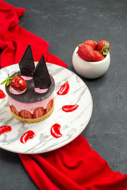 Bolo de queijo delicioso com morango e chocolate na tigela de xale vermelho com morangos em fundo escuro isolado de vista frontal