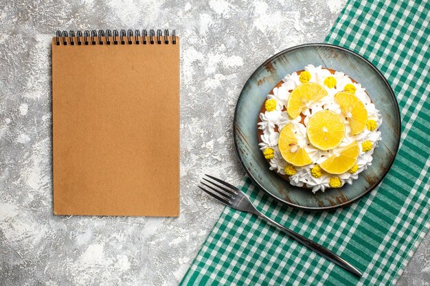 Bolo de vista superior com creme de confeiteiro e limão no garfo de prato redondo na toalha de cozinha quadriculada verde e branca. caderno vazio