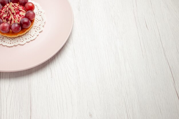 Bolo pequeno com uvas dentro do prato na mesa branca bolo de sobremesa com frutas