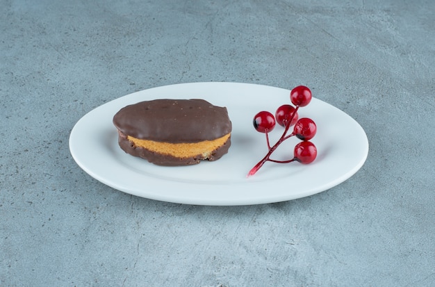 Bolo revestido de chocolate e um cacho de bagas de natal em uma travessa com fundo de mármore. foto de alta qualidade