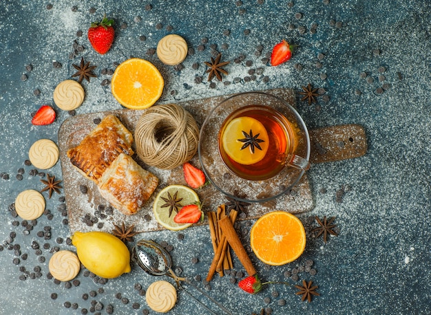 Bolos com farinha, chá, frutas, biscoitos, chips de choco, especiarias, linha em estuque e tábua de cortar, vista superior.