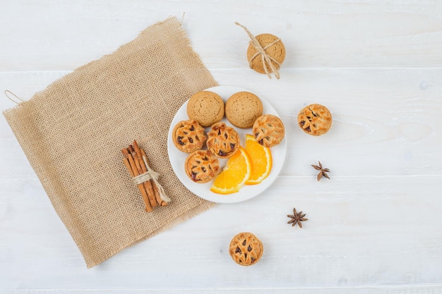 Bolos de recheio de geleia, biscoitos e laranja em um prato com canela e um jogo americano