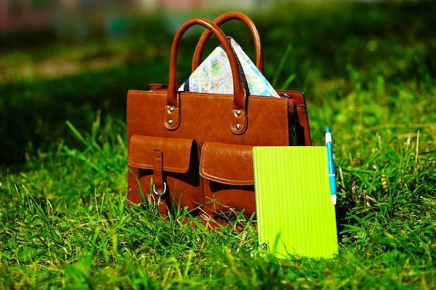 Bolsa de couro marrom retrô e notebook na grama de verão colorido brilhante no parque