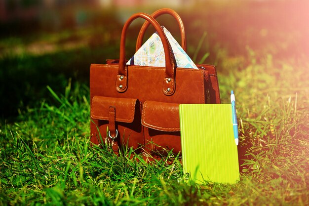 Bolsa de couro marrom retrô e notebook na grama de verão colorido brilhante no parque