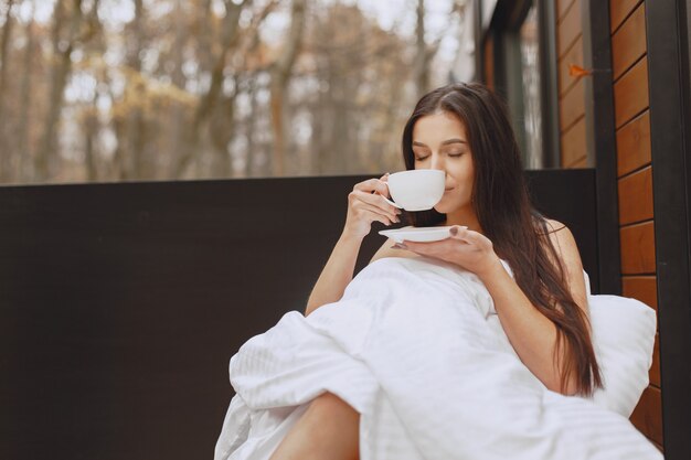 Bom Dia. Mulher em um cobertor. Senhora sentada no terraço. Morena bebe um café.