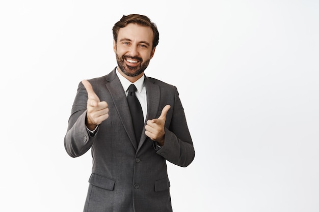 Foto grátis bom trabalho chefe sorridente apontando os dedos para a câmera mostrando os polegares para cima parecendo satisfeito com o empregado vestindo terno fundo branco