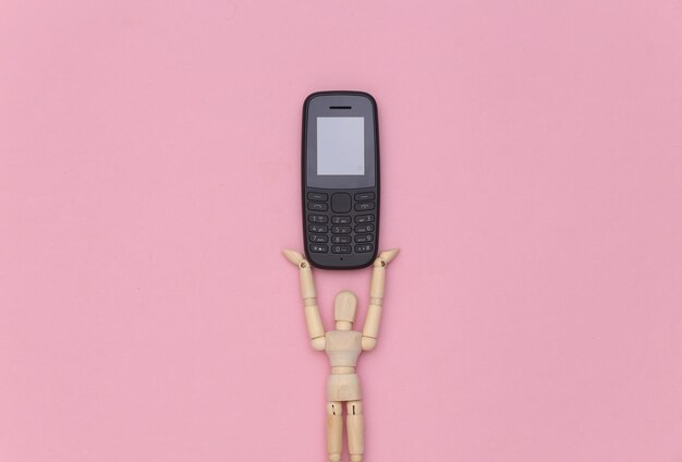 Boneco de madeira segurando um telefone com botão em um fundo rosa