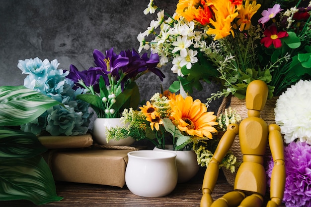 Boneco de madeira sentado em frente a flores coloridas na mesa