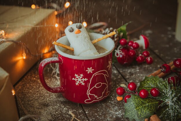 Boneco de neve na caneca de café sob chuva de pó branco