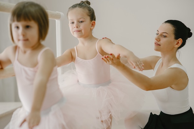 Foto grátis bonitinhas bailarinas em traje de balé rosa. crianças em sapatilhas de ponta estão dançando na sala. garoto na aula de dança com o professor.