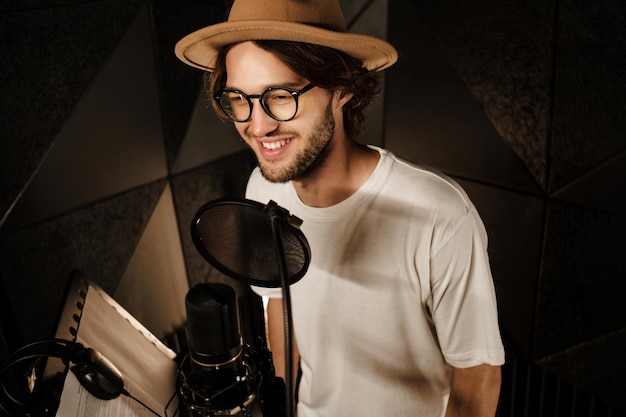 Bonito cantor masculino sorridente felizmente gravando nova música para álbum de música no estúdio de som moderno
