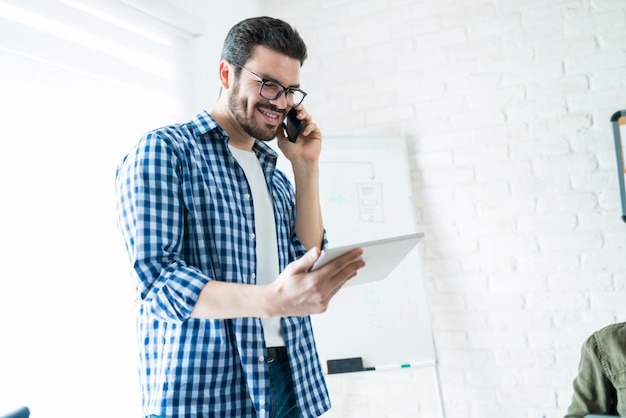 Bonito empresário latino discutindo sobre tablet digital no smartphone no escritório