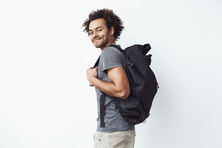Foto grátis bonito homem africano com mochila sorrindo em pé no perfil.