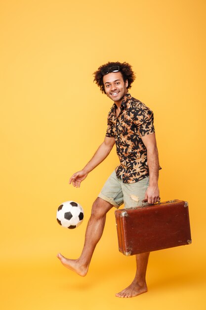 Bonito homem Africano em pé e segurando a mala e futebol