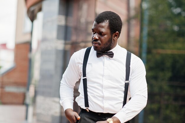 Bonito homem afro-americano elegante com roupa formal, gravata borboleta e suspensórios bengala