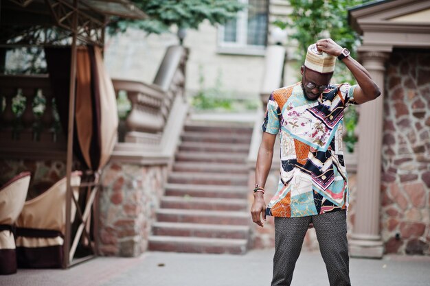 Bonito homem afro-americano vestindo boné de roupas tradicionais e óculos na cidade moderna