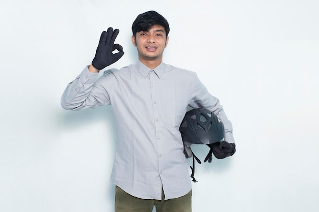 Bonito homem asiático com um capacete de motocicleta mostrando um gesto de ok com o polegar para cima no fundo branco Foto Premium