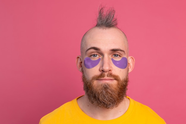 Bonito homem barbudo europeu com camiseta amarela e tapa-olhos roxos máscara rosa