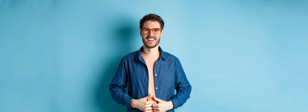 Bonito homem barbudo sorrindo satisfeito usando óculos novos em pé no fundo azul