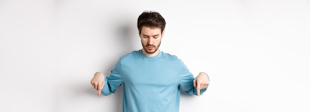 Bonito homem caucasiano com barba vestindo camisa azul olhando e apontando para o logotipo interessante b