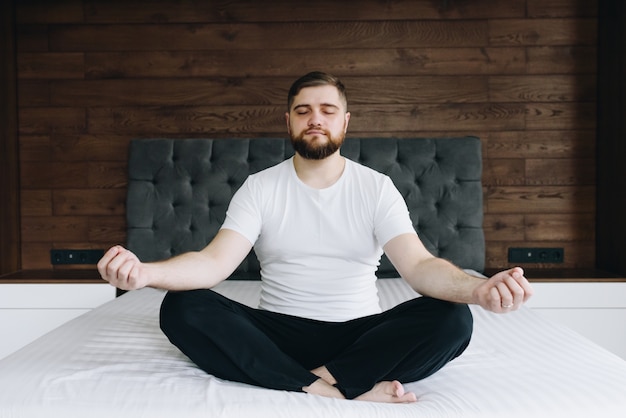 Bonito homem caucasiano meditando e estar atento em sua cama no quarto
