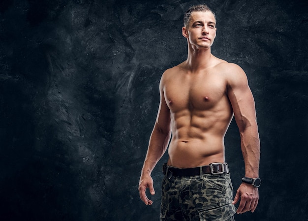 Bonito homem musculoso sem camiseta está posando para fotógrafo no estúdio fotográfico escuro.