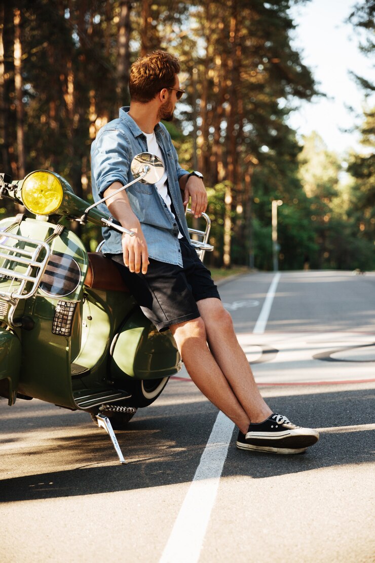 Foto grátis bonito jovem barbudo em pé perto de scooter ao ar livre