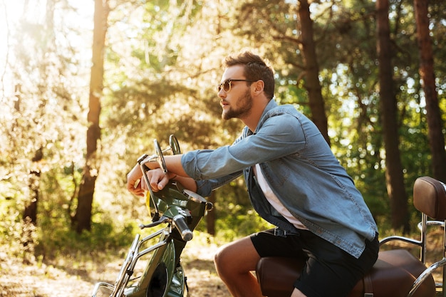 Bonito jovem barbudo sentado na scooter ao ar livre