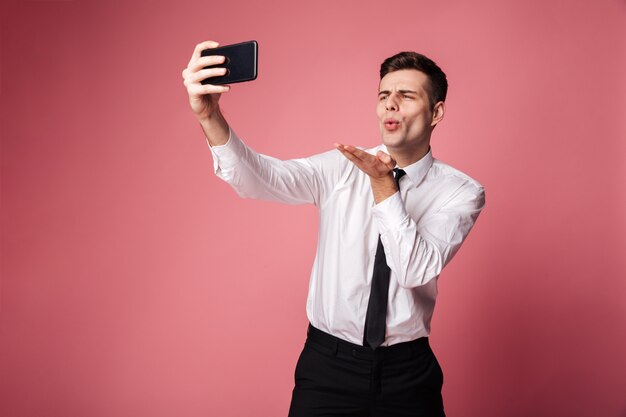 Bonito jovem empresário fazer selfie pelo celular soprando beijos.