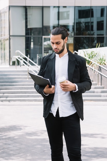 Foto grátis bonito, jovem, homem negócios, segurando, descartável, copo papel, olhar clipboard