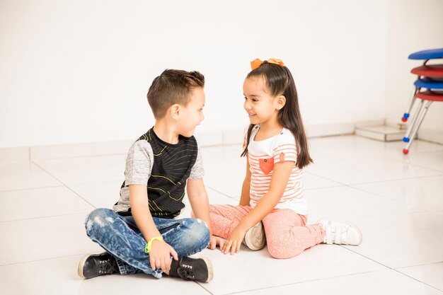 Bonito menino e menina sentados cara a cara no chão da sala de aula e flertando um com o outro