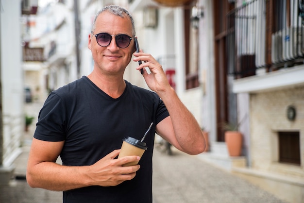 Bonito no telefone. Jovem apaixonado por um traje casual inteligente falando no celular e desviando o olhar enquanto fica na rua