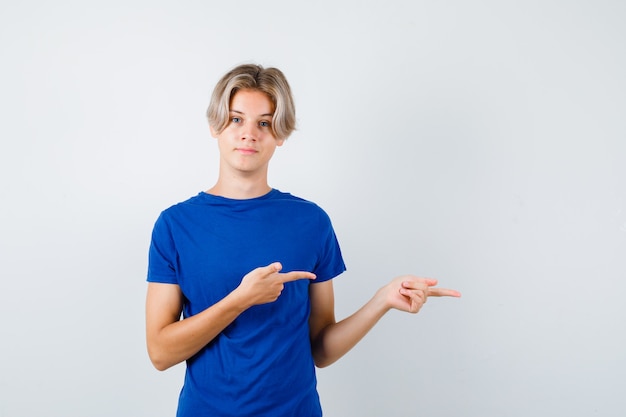 Bonito rapaz adolescente apontando para a direita em t-shirt azul e parecendo confiante. vista frontal.