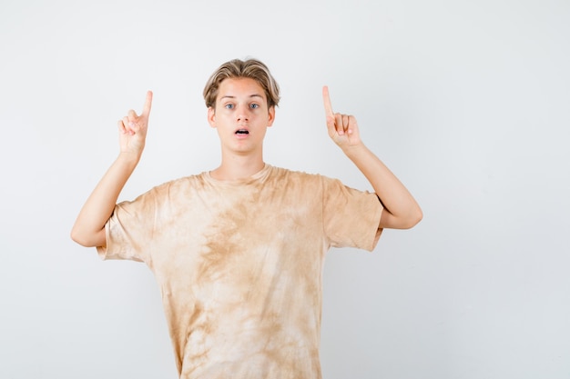 Bonito rapaz adolescente apontando para cima em t-shirt e parecendo perplexo. vista frontal.