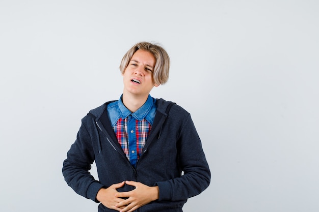 Bonito rapaz adolescente com camisa, moletom com capuz, sofrendo de dor de estômago e parecendo incomodado, vista frontal.