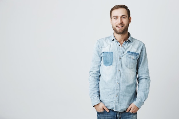 Foto grátis bonito rapaz barbudo na camisa jeans de mãos dadas nos bolsos