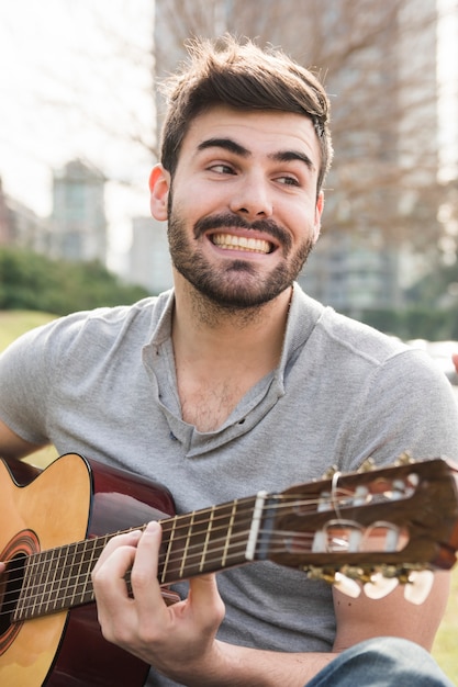 Foto grátis bonito, sorrindo, homem jovem, violão jogo, em, ao ar livre