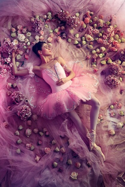 Bons sonhos. Vista superior de uma bela jovem em tutu de balé rosa rodeada por flores. Humor de primavera e ternura à luz coral.