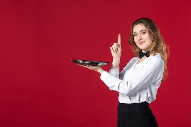 Foto grátis borboleta servidor feminino no pescoço segurando a bandeja apontando para cima no fundo vermelho