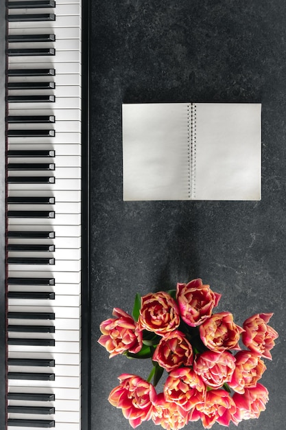 Bouquet de piano de flores de tulipa e bloco de notas em um fundo escuro vista superior