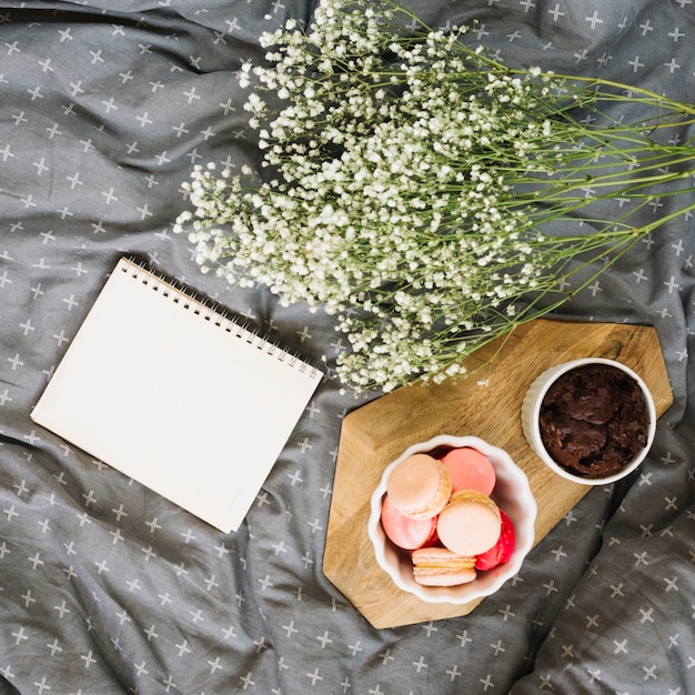 Bouquet perto de bloco de notas e sobremesas na cama