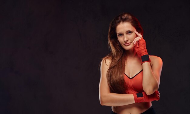 Boxer feminino morena linda pensativa no sutiã esportivo com as mãos enfaixadas. Isolado em um plano de fundo texturizado escuro.