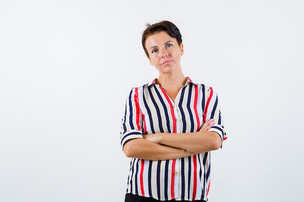 Braços em pé de mulher madura cruzados em uma camisa listrada e parecendo confiante. vista frontal.