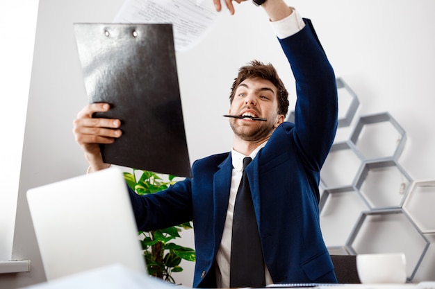 Foto grátis bravo jovem empresário sentado no local de trabalho, plano de fundo do escritório.