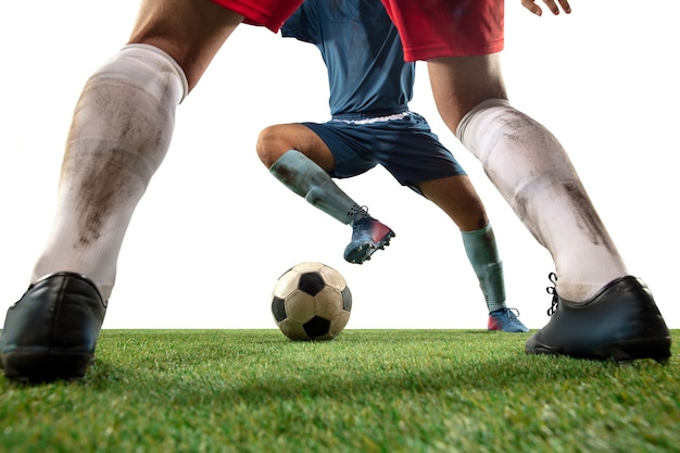 Brigando. Feche as pernas do futebol profissional, jogadores de futebol lutando pela bola em campo isolado na parede branca. Conceito de ação, movimento, emoção de alta tensão durante o jogo. Imagem recortada.